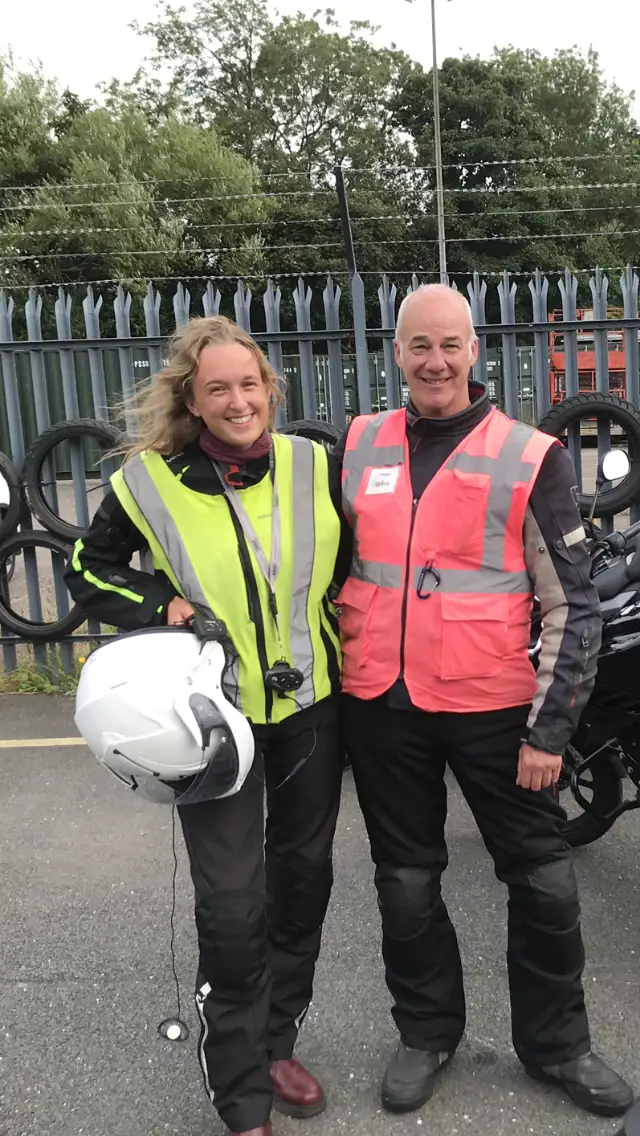 A student holding her helmet standing with her instructor